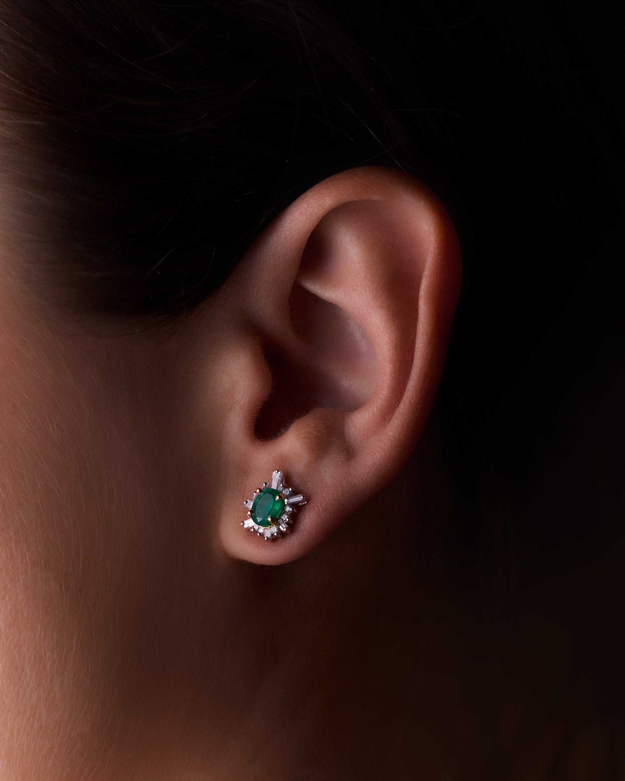 Oval-cut emerald sunburst earrings with white diamonds in yellow gold, radiant and elegant design, worn on model.