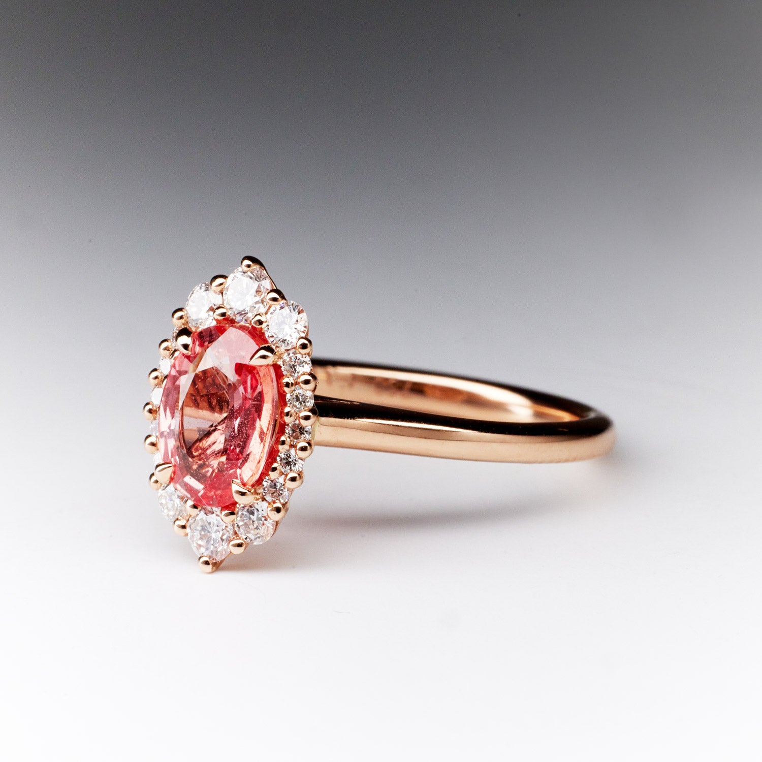 Unique Oval Padparadscha sapphire ring with round diamond halo, 18k rose gold setting.