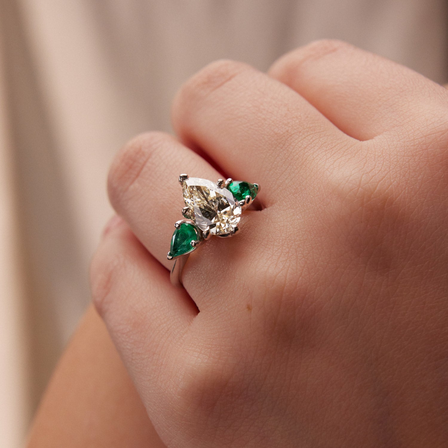 Faith Jewels Belle Époque engagement ring with a pear-cut M-colour diamond center, flanked by pear-cut emeralds, set in 18k white gold with elegant sweeping claws