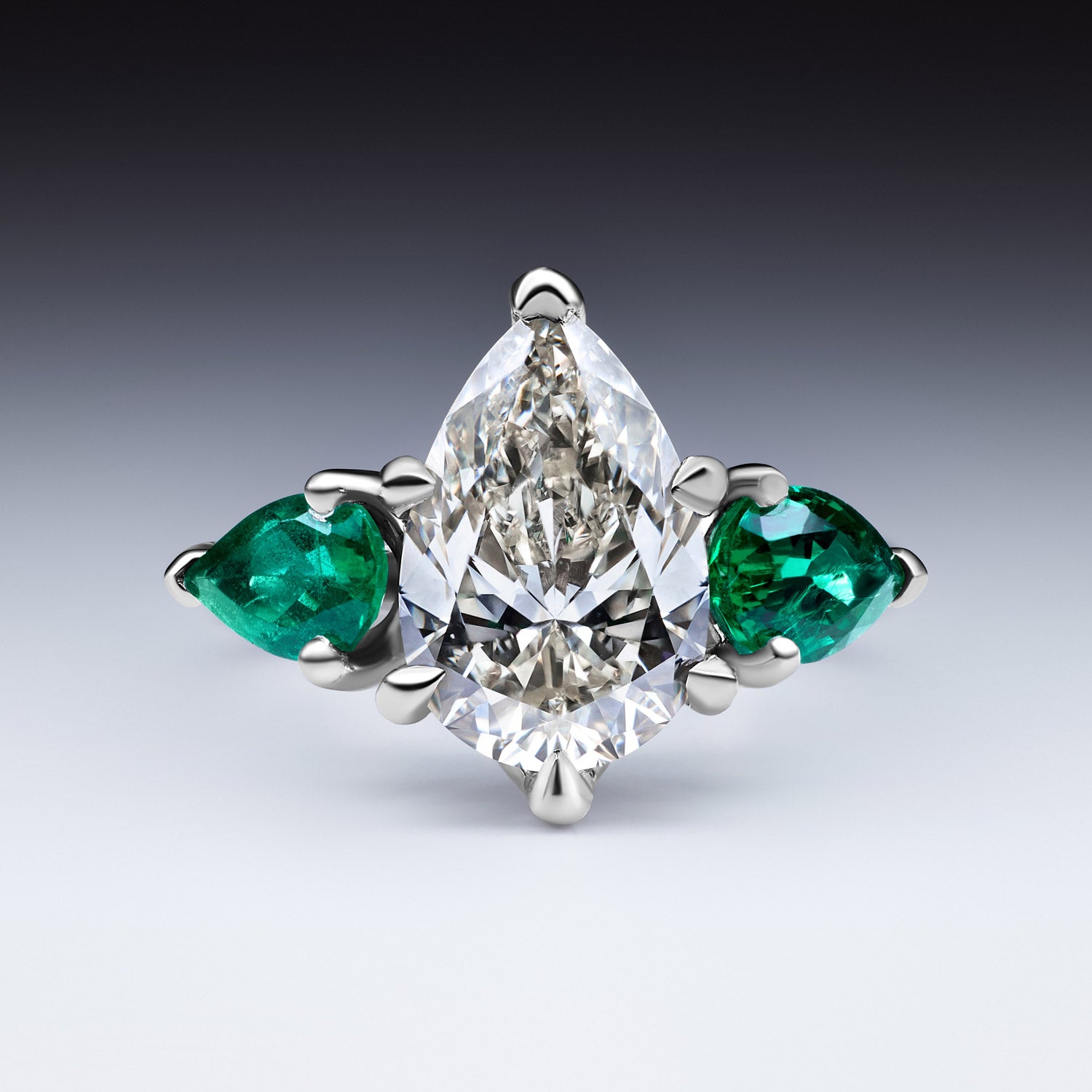 Faith Jewels Belle Époque engagement ring with a pear-cut diamond center, flanked by pear-cut emeralds, set in 18k white gold with elegant sweeping claws
