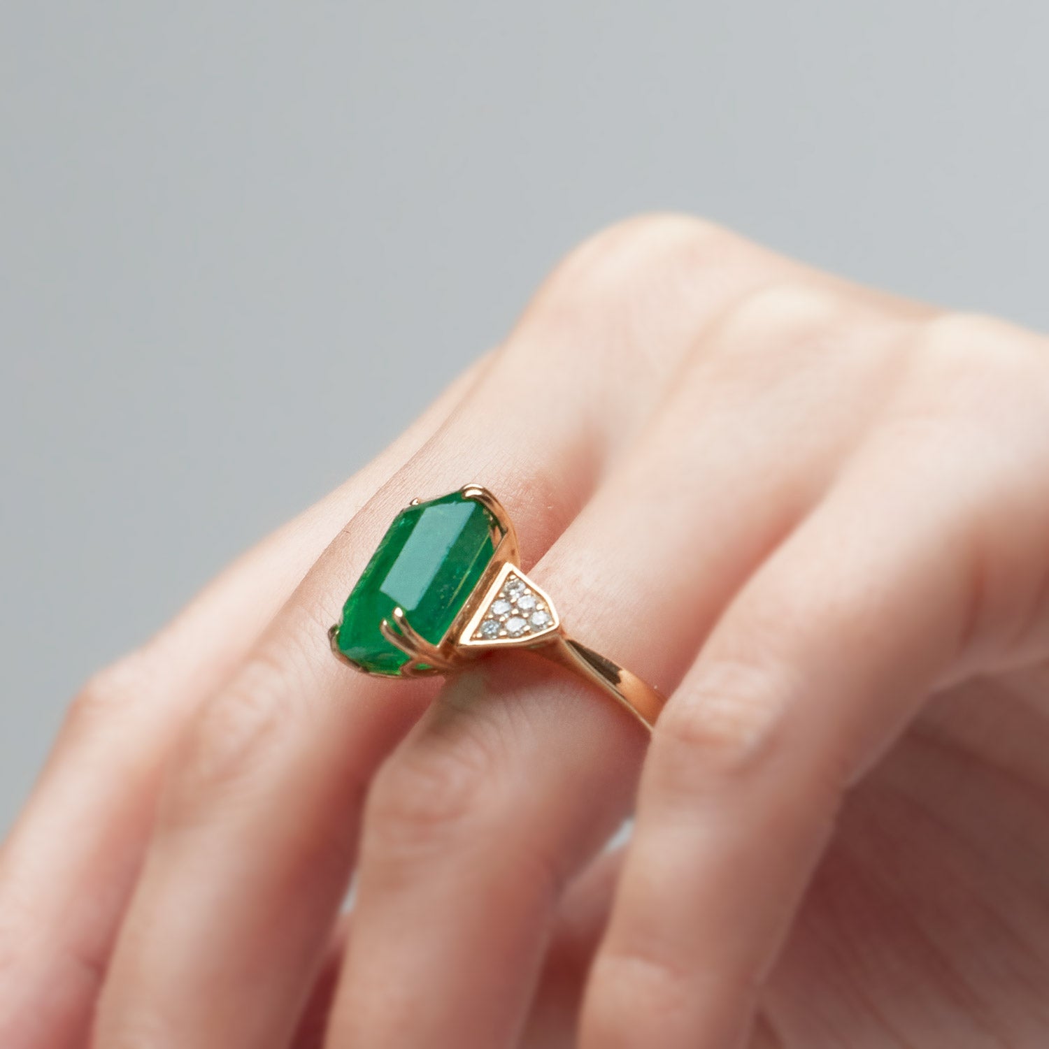 Emerald-cut emerald ring with grain-set diamond accents, set in a yellow gold band.