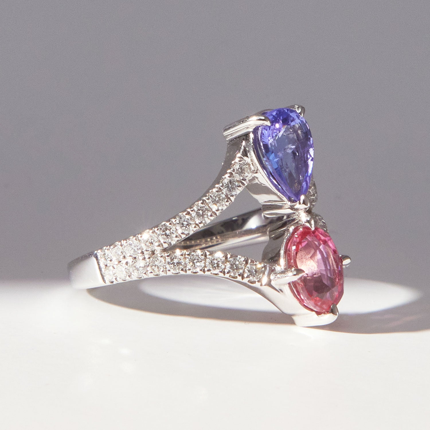 Faith Jewels Elsie ring in 18k white gold featuring a pear-cut tanzanite and a pink sapphire, set on a split diamond white gold band
