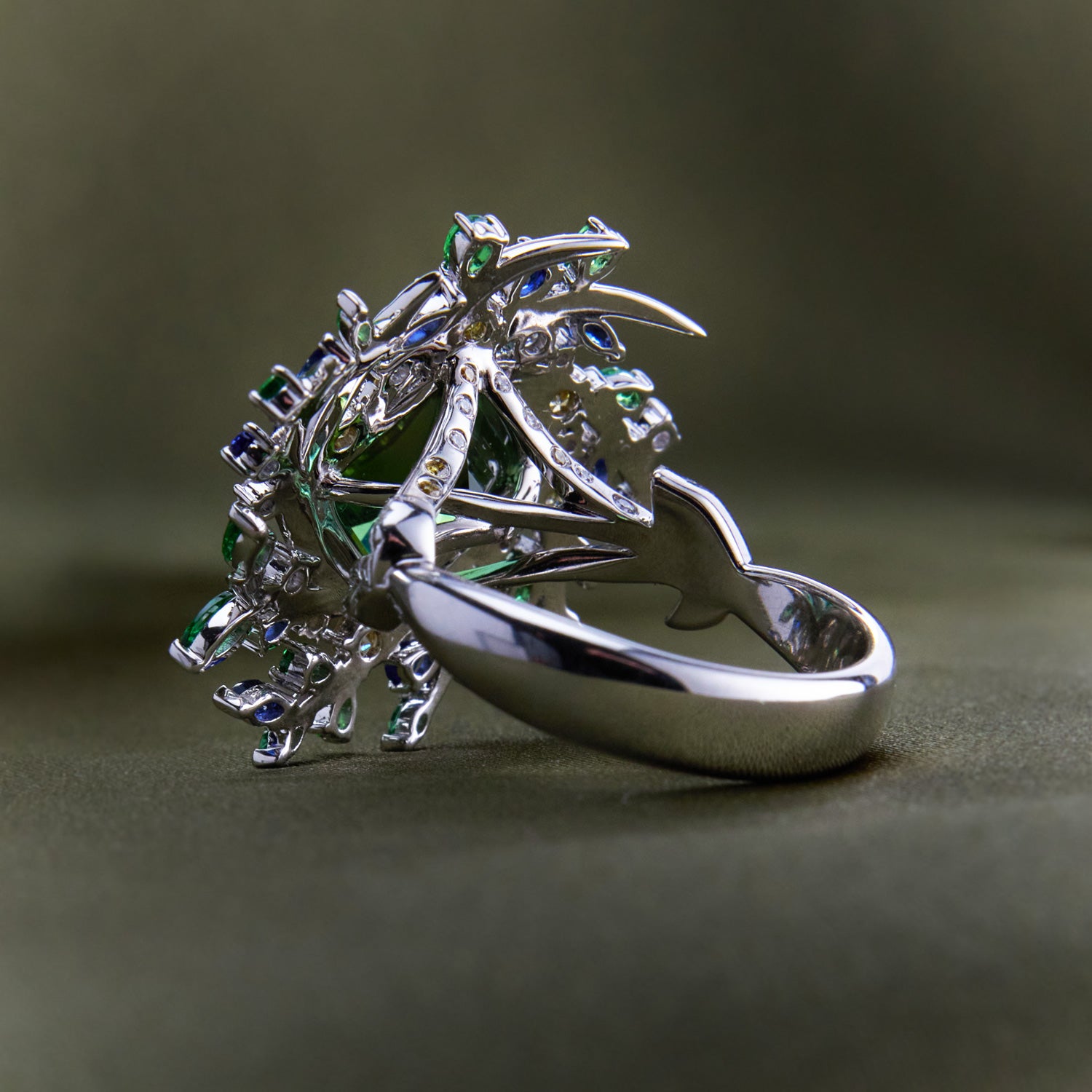Nature-inspired ring with twig-like branches holding a vibrant mix of green, blue, and yellow sapphires and diamonds in white gold band