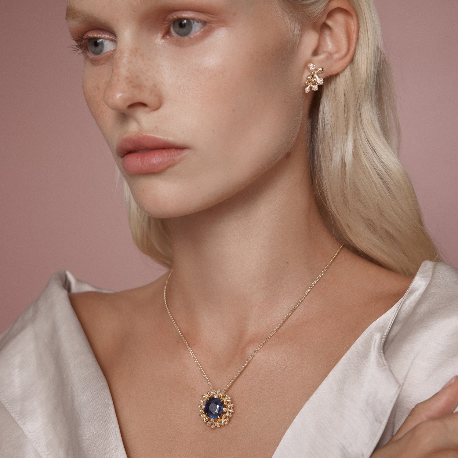 A luxurious interchangeable necklace and ring set featuring a royal blue Ceylon sapphire, surrounded by a floral wreath of golden florals with white diamonds, all in 18k yellow gold.