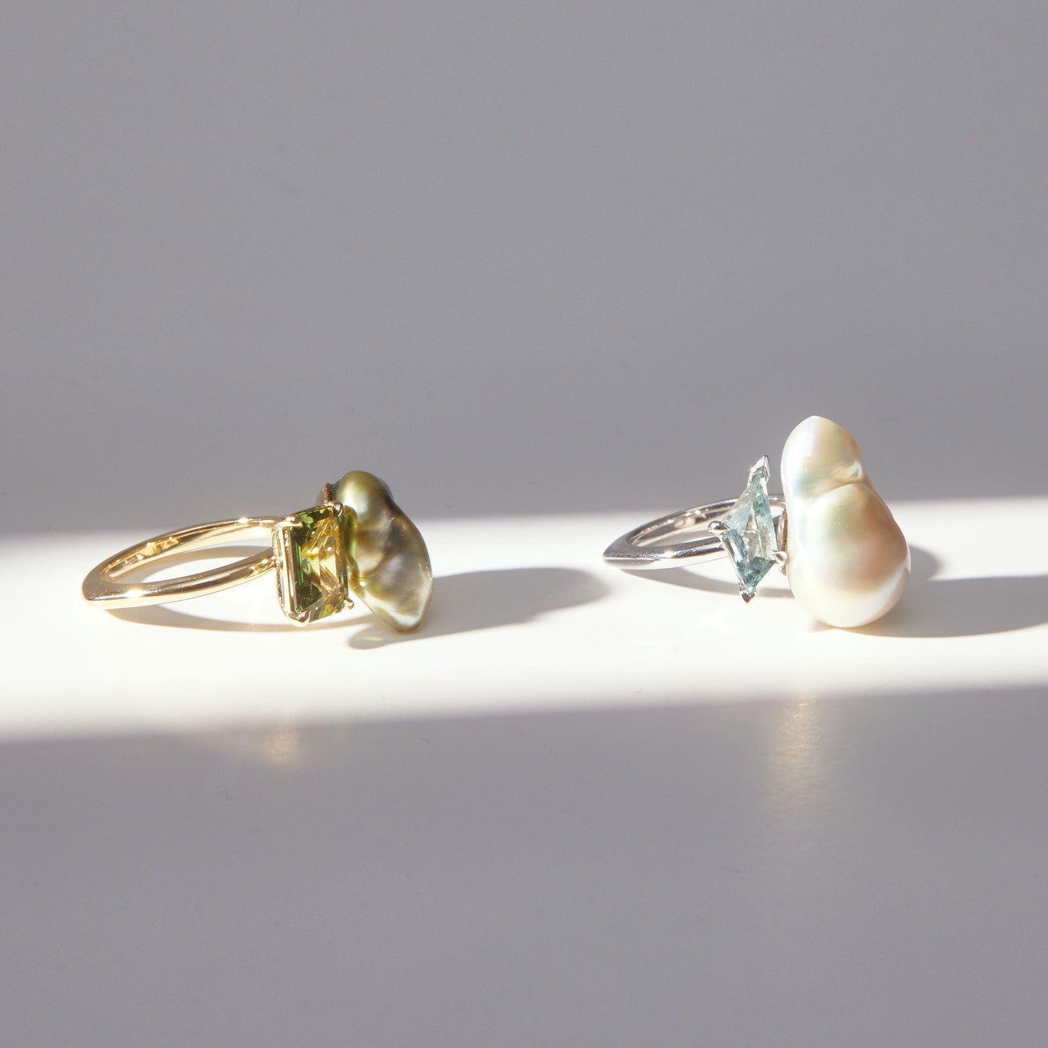 Faith Jewels Toi et Moi ring featuring a baroque pearl and tourmaline set in an 18k yellow gold band and another featuring a baroque pearl and fancy kite-cut aquamarine set in an 18k white gold band