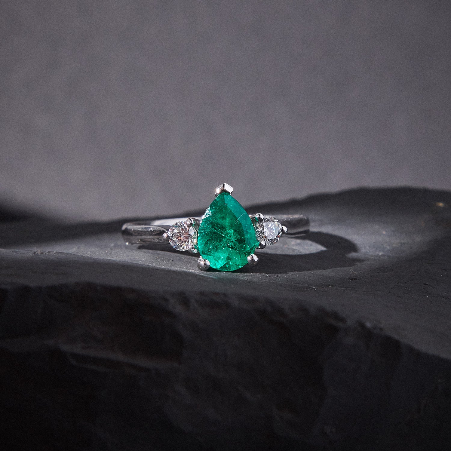 Pear-cut emerald trilogy ring with round white diamonds in 18k white gold, elegant and timeless design.
