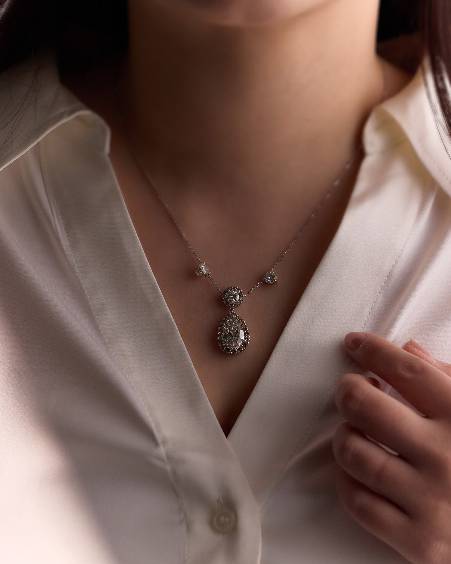 Elegant diamond necklace featuring round brilliant pendant with pear-shaped drop and champagne halo on model