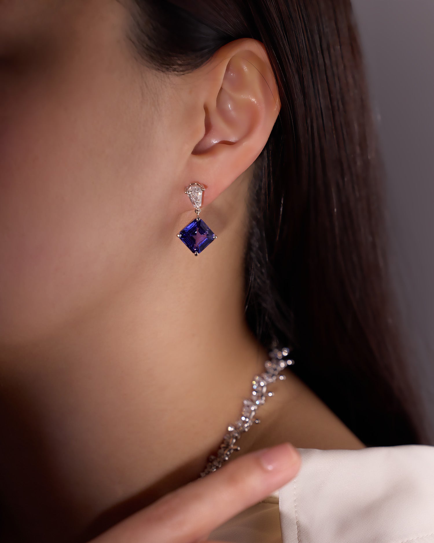 Bespoke tanzanite earrings with pear-shaped white diamond accents, set in white gold and worn on model