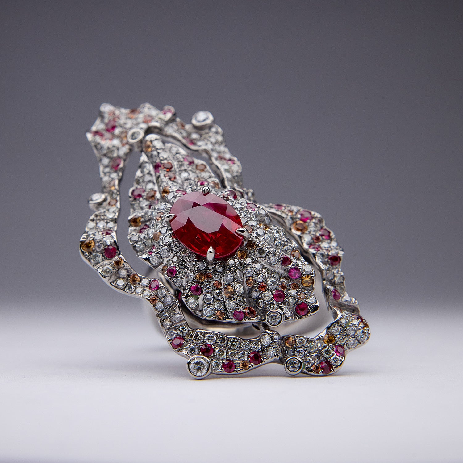 The Inferno Ring with Burmese ruby, diamonds, and orange sapphires in grey titanium, fiery and sculptural design.