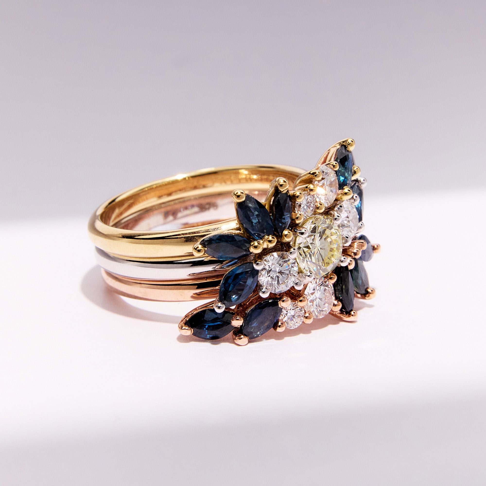 Custom and elegant three-generation heirloom ring set with diamonds and marquise blue sapphires in white, rose, and yellow gold, side view.