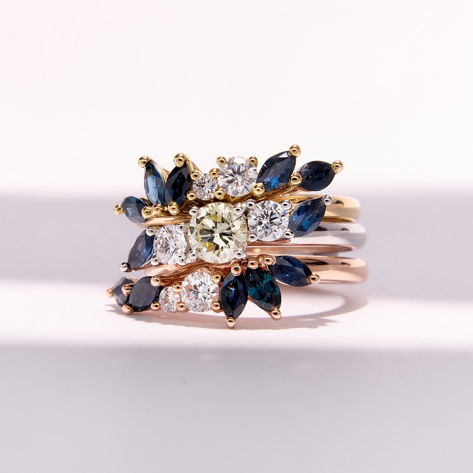 Custom and elegant three-generation heirloom ring set with diamonds and marquise blue sapphires in white, rose, and yellow gold