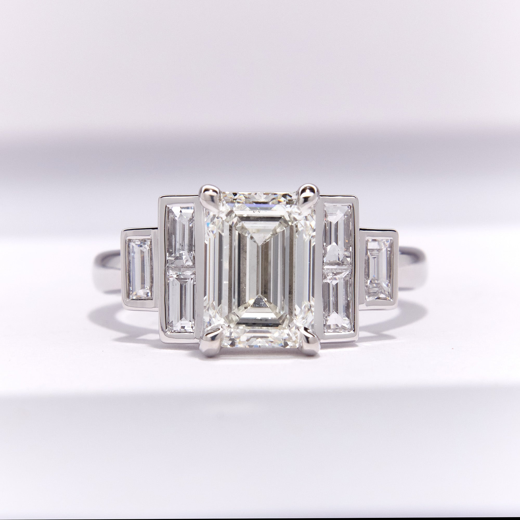 Diamond engagement ring with emerald-cut center stone and baguette side stones on a white background
