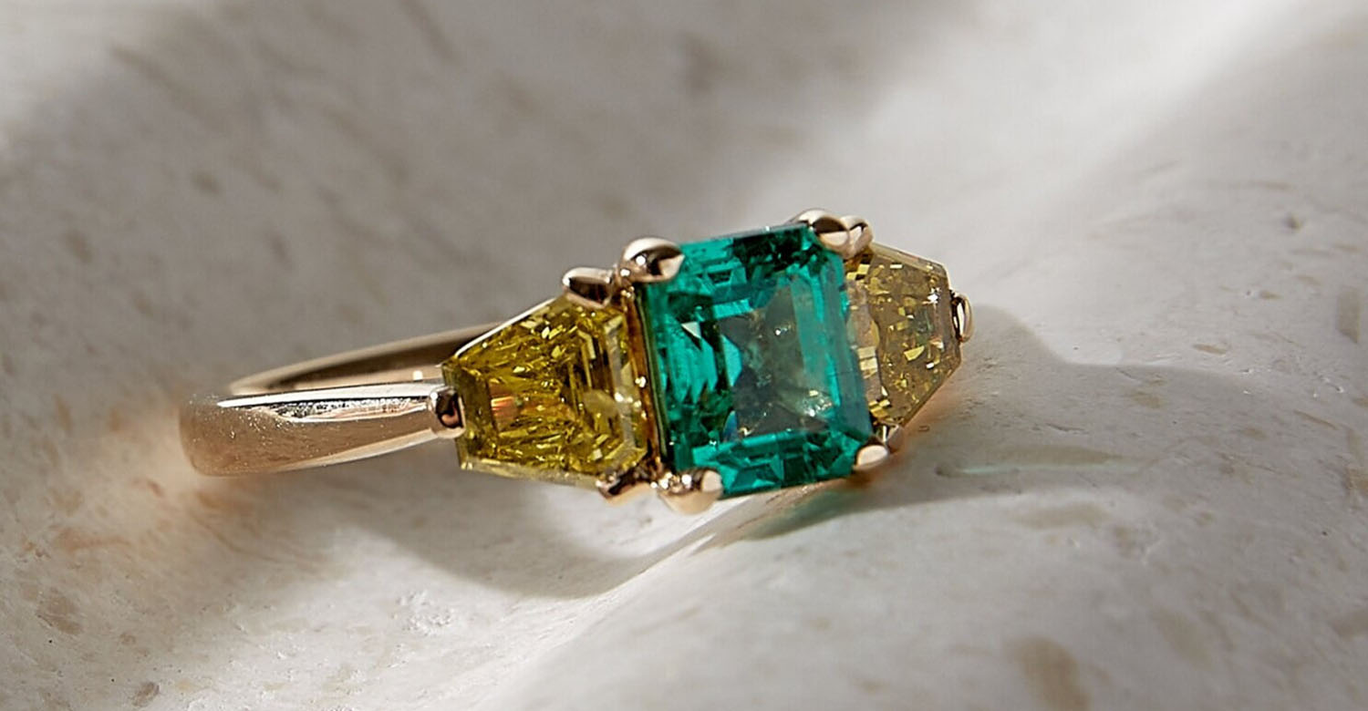 Gold ring with green and yellow gemstones on a textured surface