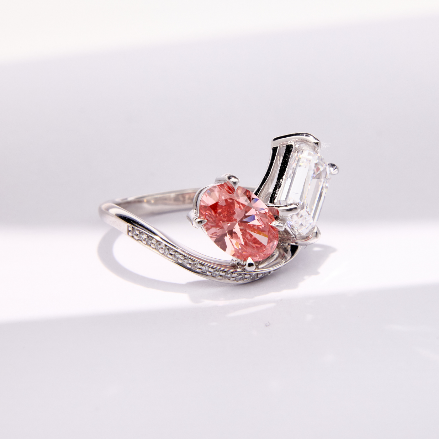 Unique Faith Jewels bespoke white gold ring with a pink oval-cut diamond and white emerald-cut diamond in an asymmetric, pavé diamond setting.