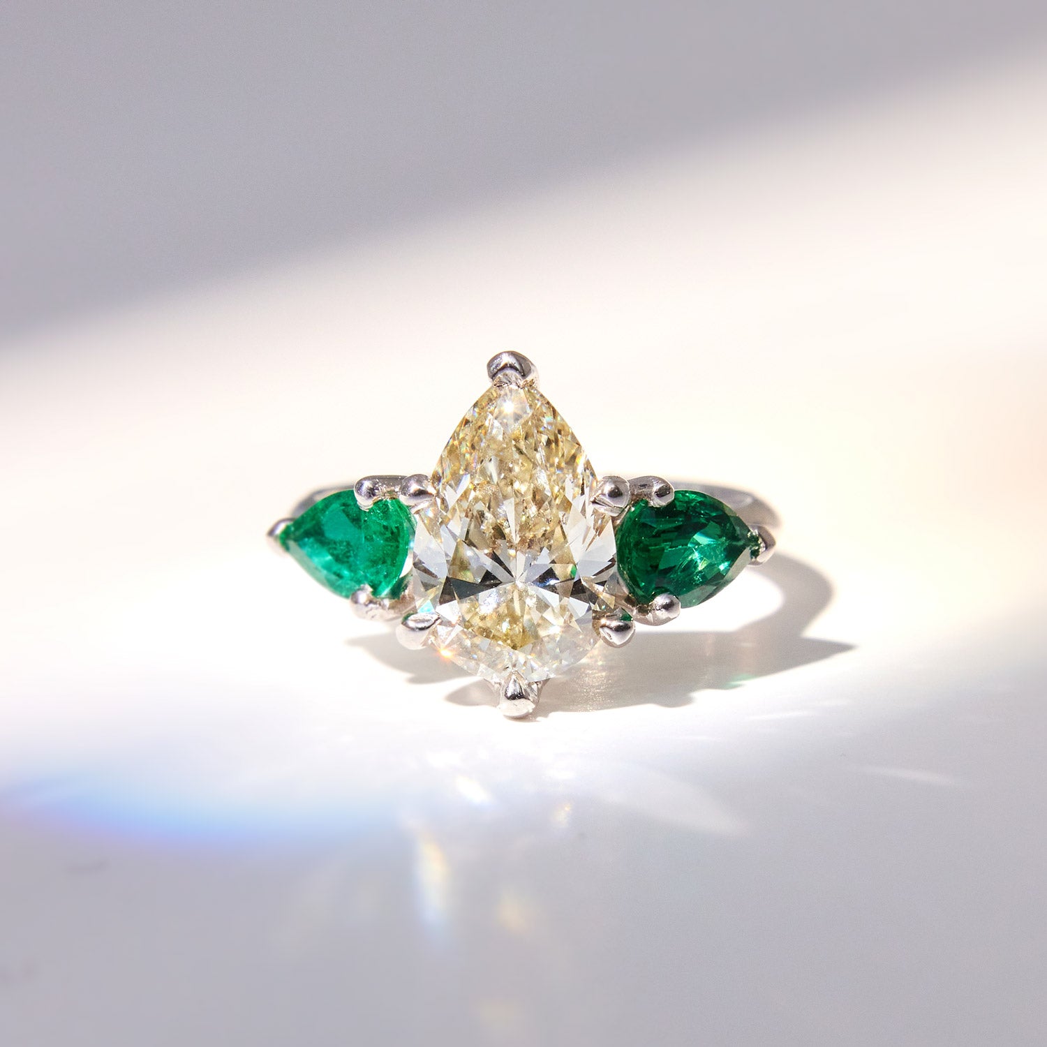 Faith Jewels Belle Époque engagement ring with a pear-cut M-colour diamond center, flanked by pear-cut emeralds, set in 18k white gold with elegant sweeping claws