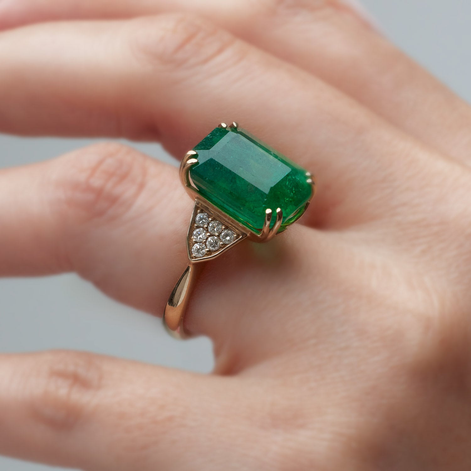 Emerald-cut emerald ring with grain-set diamond accents, set in a yellow gold band.