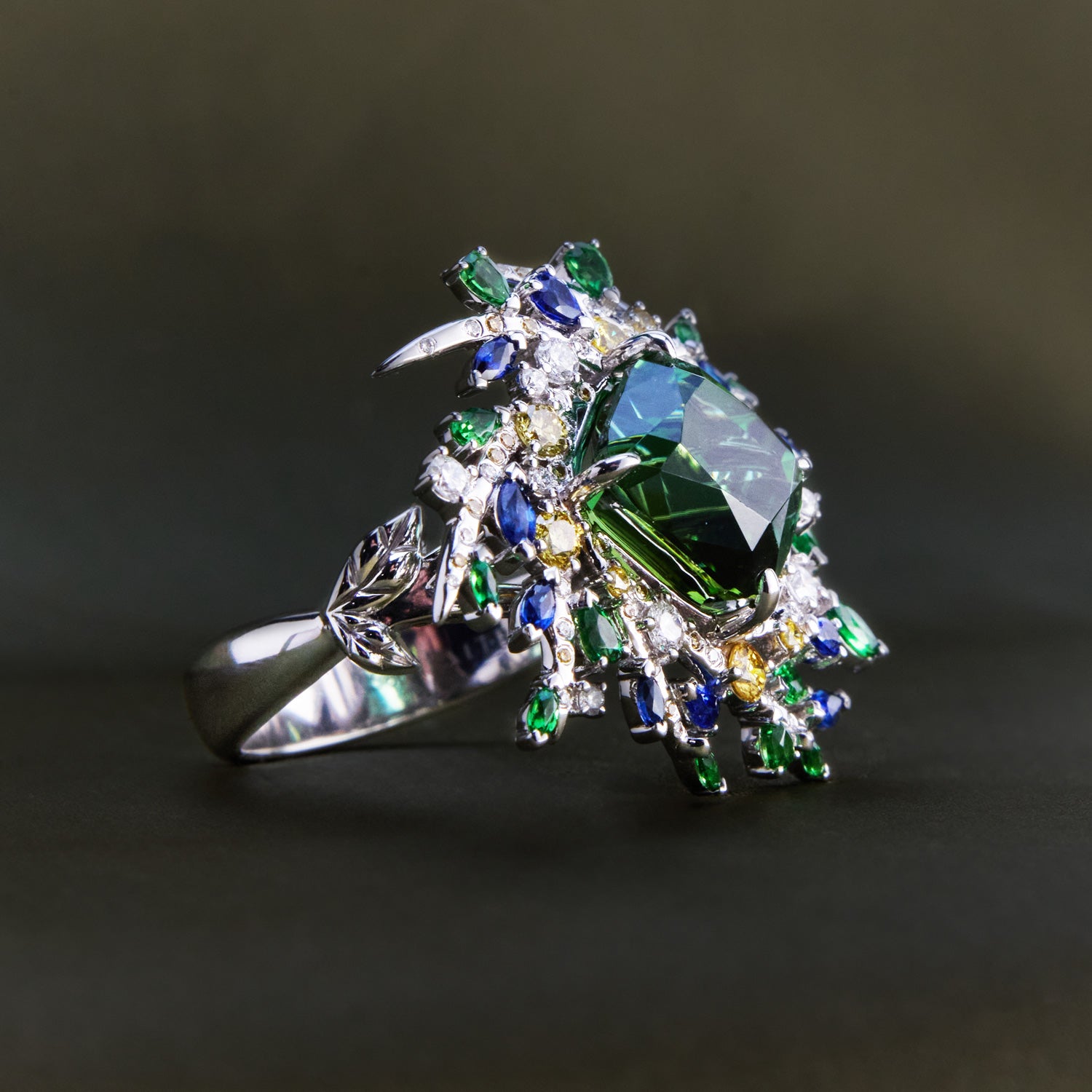 Nature-inspired ring with twig-like branches holding a vibrant mix of green, blue, and yellow sapphires and diamonds in white gold band