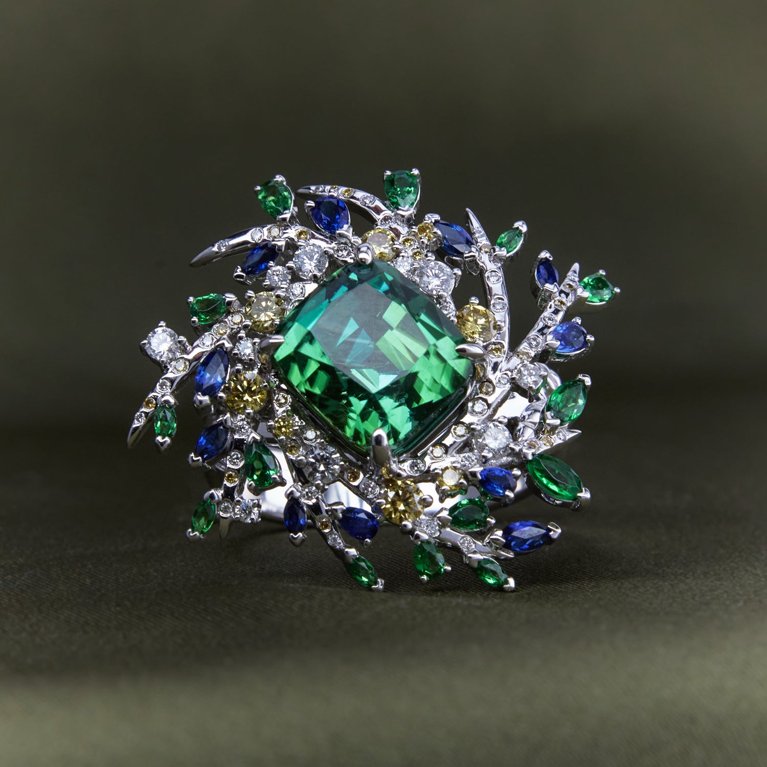 Nature-inspired ring with twig-like branches holding a vibrant mix of green, blue, and yellow sapphires and diamonds in white gold band