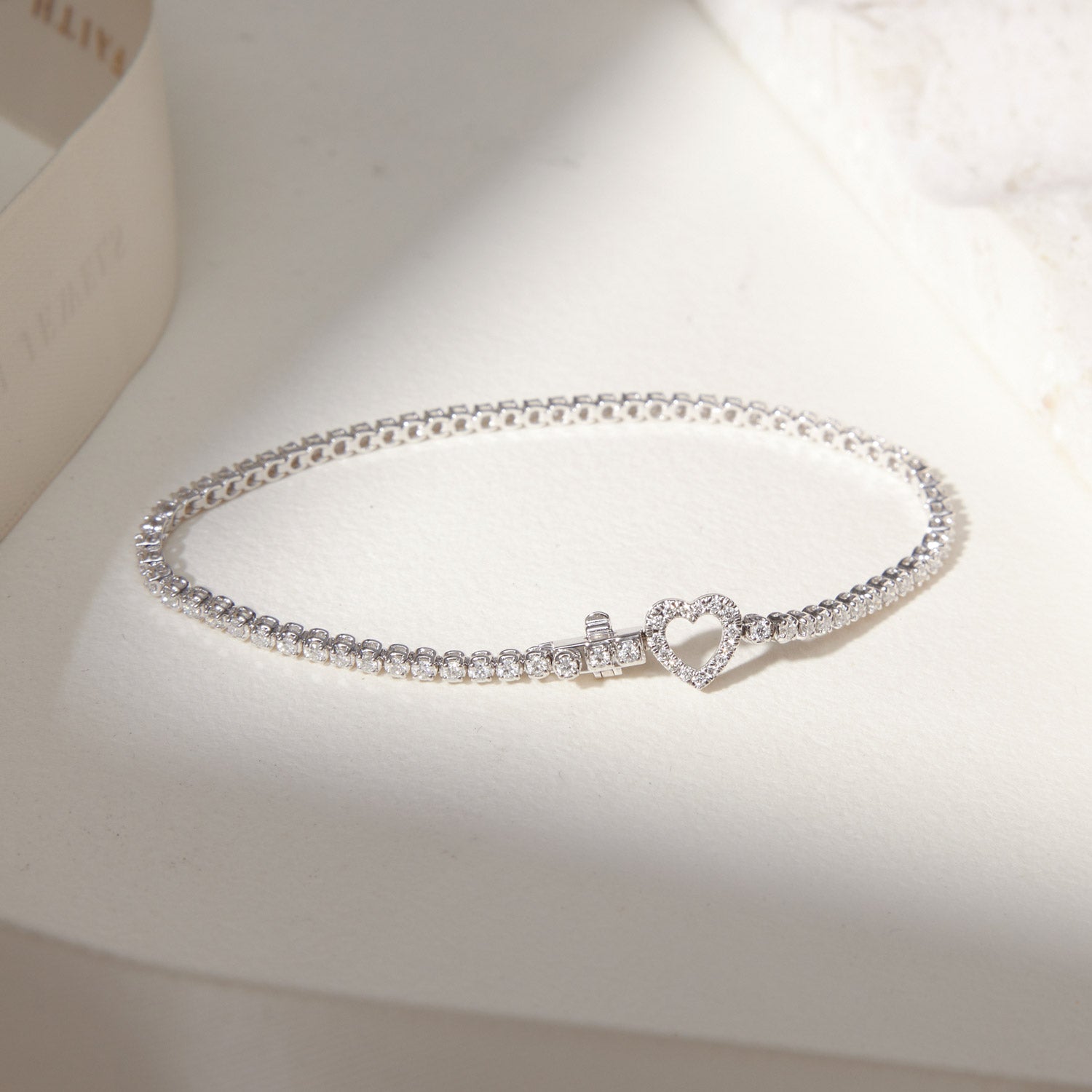 Faith Jewels bespoke initial diamond tennis bracelets in white gold, each featuring a unique clasp shaped as a heart symbol — set with round brilliant-cut diamonds