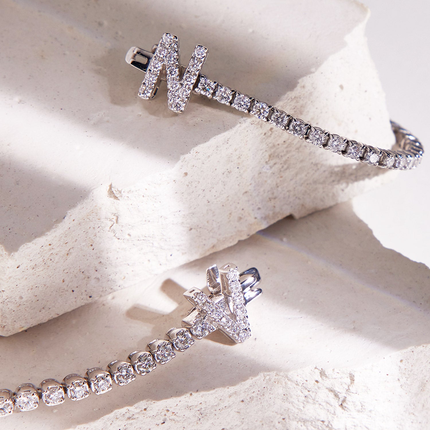Faith Jewels bespoke initial diamond tennis bracelets in white gold, each featuring a unique clasp shaped as a letter  N and V — set with round brilliant-cut diamonds