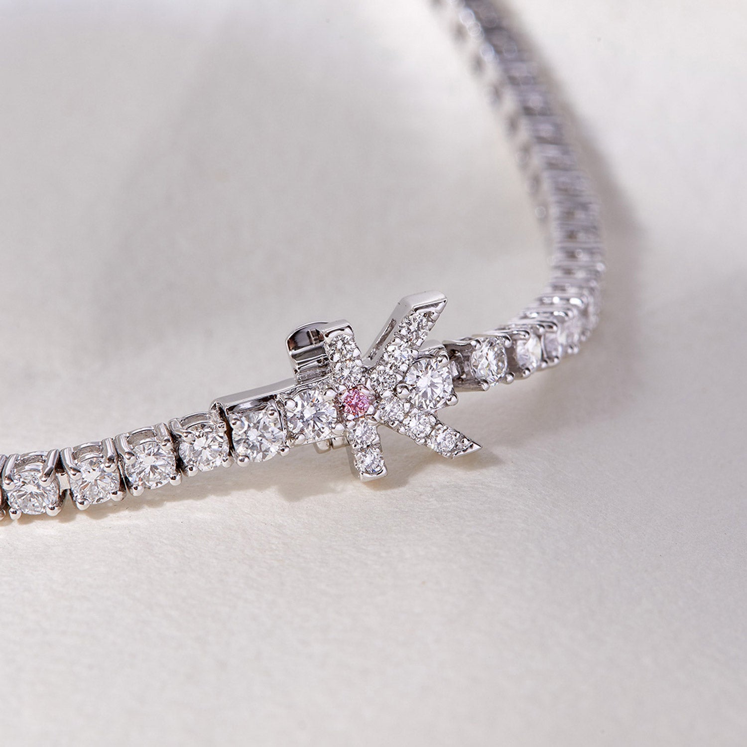 Faith Jewels bespoke initial diamond tennis bracelets in white gold, each featuring a unique clasp shaped as a letter K — set with round brilliant-cut diamonds and accent argyle pink stone