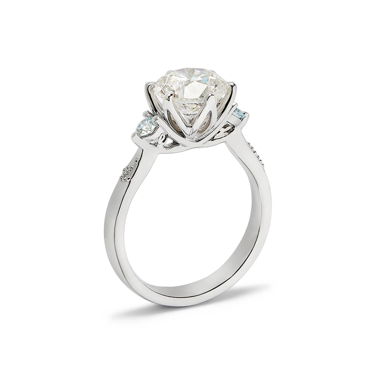 Faith Jewels Lotus engagement ring featuring a round brilliant-cut diamond flanked by two pear-cut aquamarines on a tapered band, with personalised initials underneath the stones