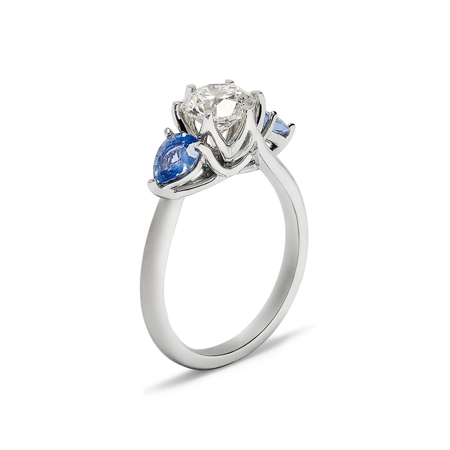 Faith Jewels Lotus engagement ring featuring a round brilliant-cut diamond flanked by two pear-cut blue sapphires on a tapered white gold band, inspired by the lotus flower