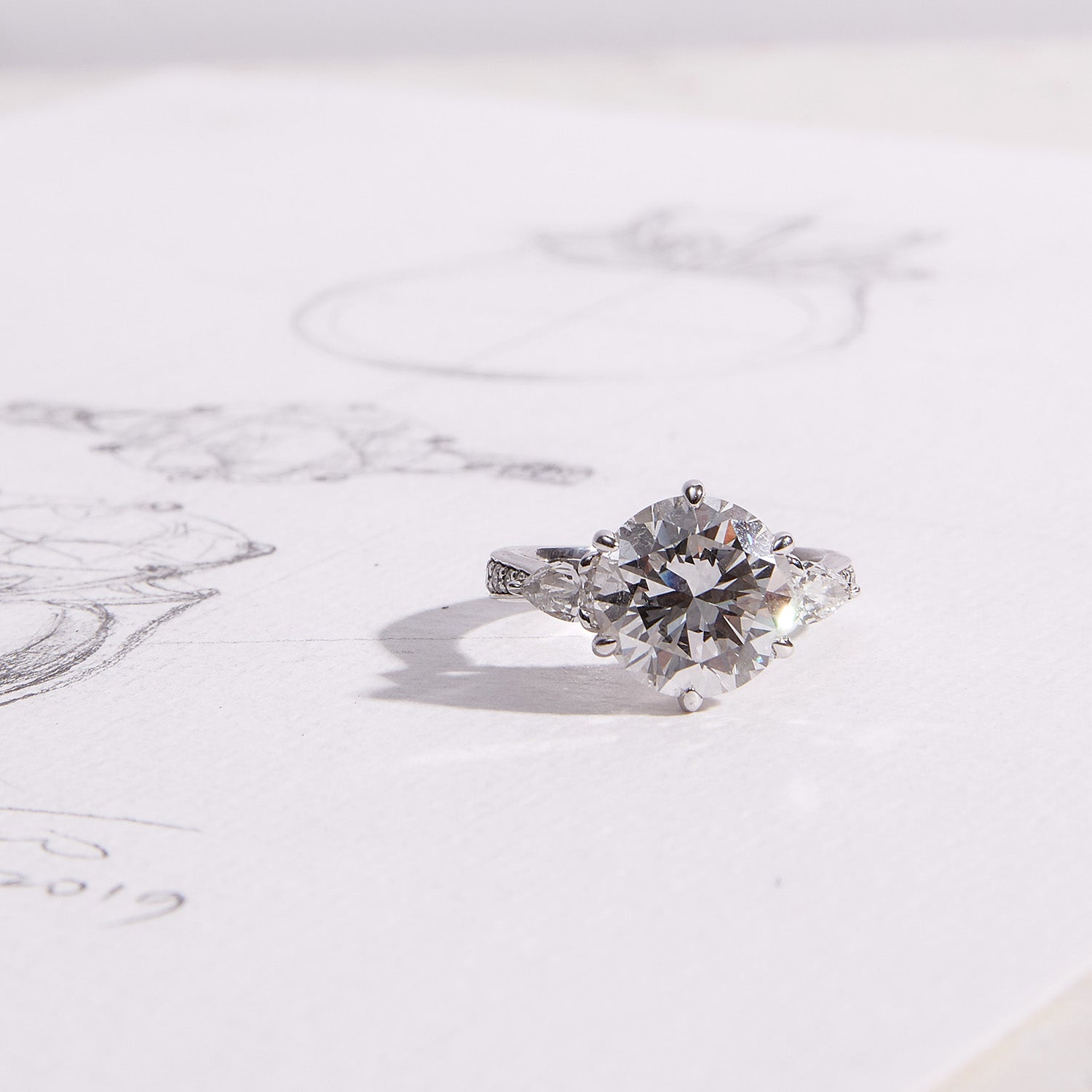 Faith Jewels Lotus engagement ring featuring a round brilliant-cut diamond flanked by two pear-cut diamonds on a tapered pavé diamond band, inspired by the lotus flower