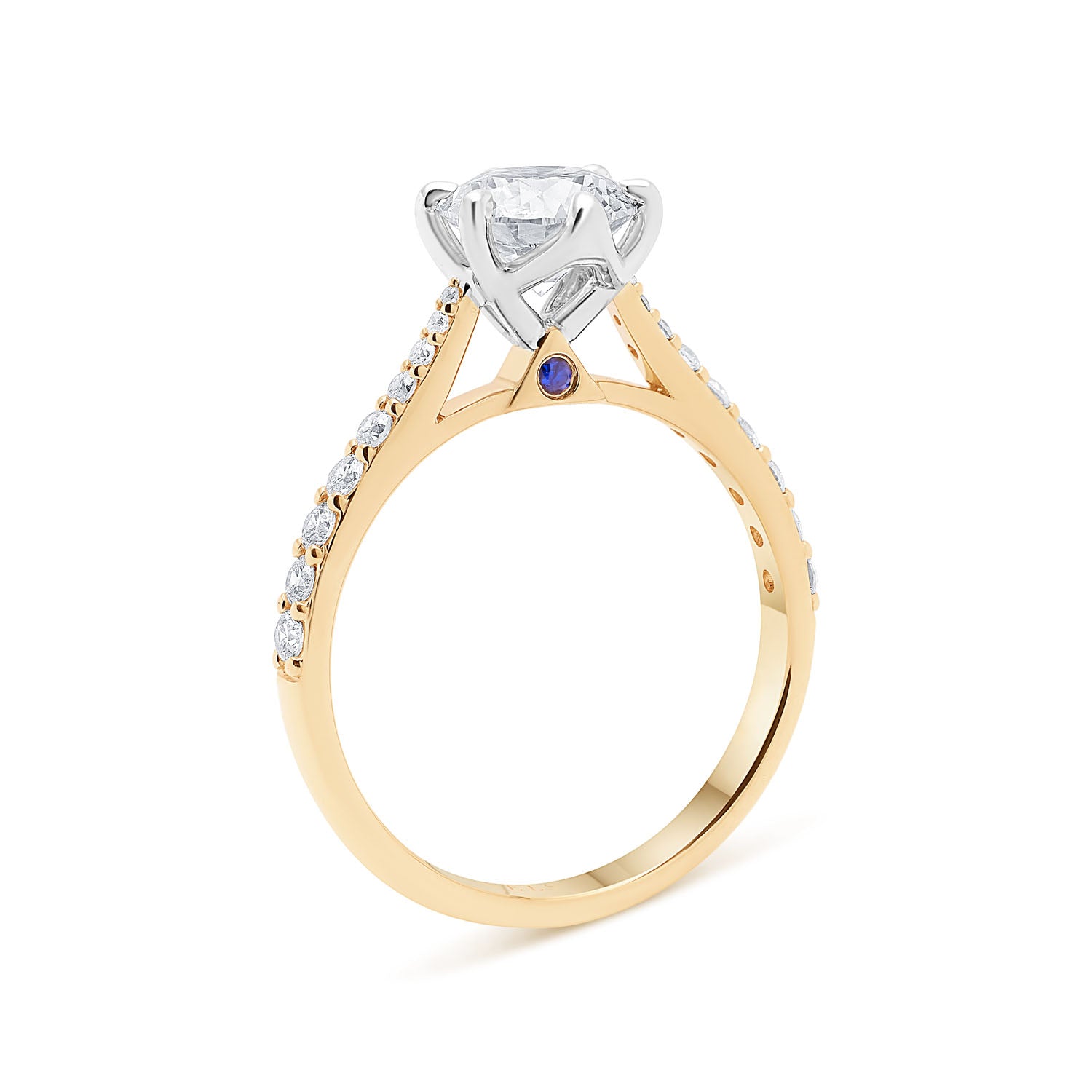 Faith Jewels Miriam diamond engagement ring featuring a round cut diamond solitaire with a blue sapphire beneath, set in a diamond-accented 18k yellow gold band