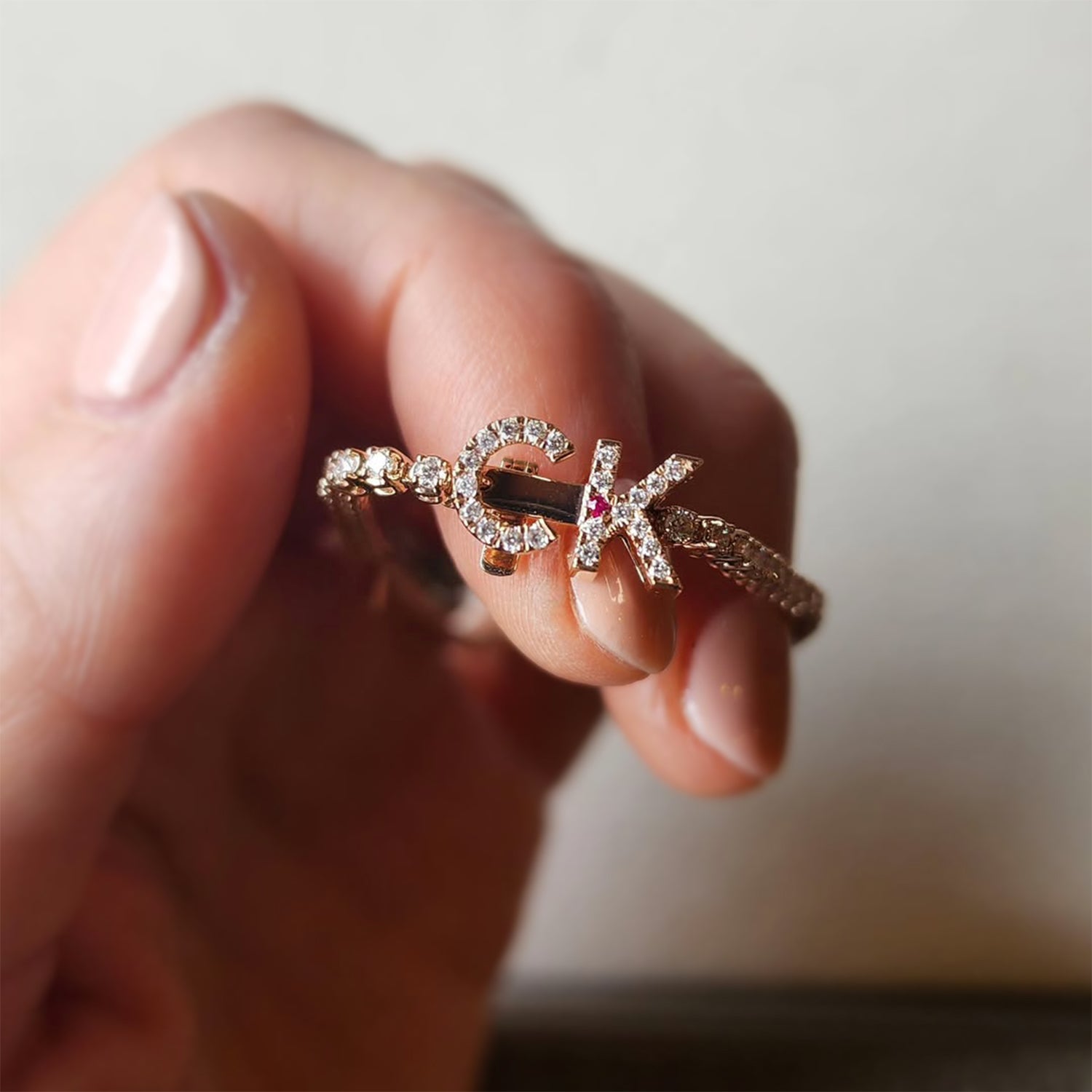 Faith Jewels bespoke initial diamond tennis bracelets in rose gold, each featuring a unique clasp shaped as a letter C and K — set with round brilliant-cut diamonds and red ruby