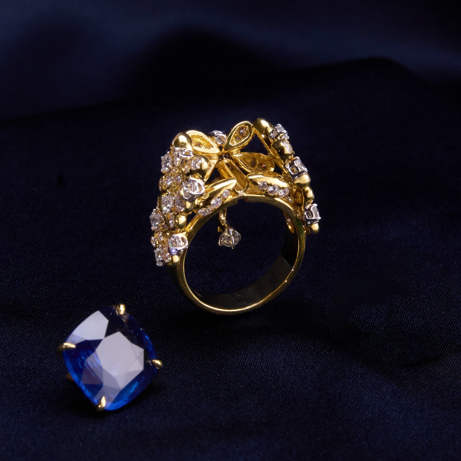 A luxurious interchangeable necklace and ring set featuring a royal blue Ceylon sapphire, surrounded by a floral wreath of golden florals with white diamonds, all in 18k yellow gold.