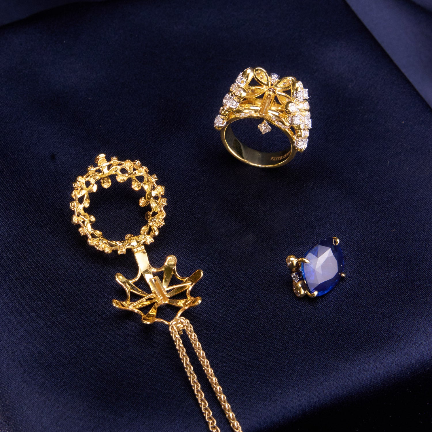 A luxurious interchangeable necklace and ring set featuring a royal blue Ceylon sapphire, surrounded by a floral wreath of golden florals with white diamonds, all in 18k yellow gold.