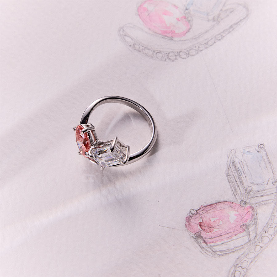 Unique Faith Jewels bespoke white gold ring with a pink oval-cut diamond and white emerald-cut diamond in an asymmetric, pavé diamond setting.