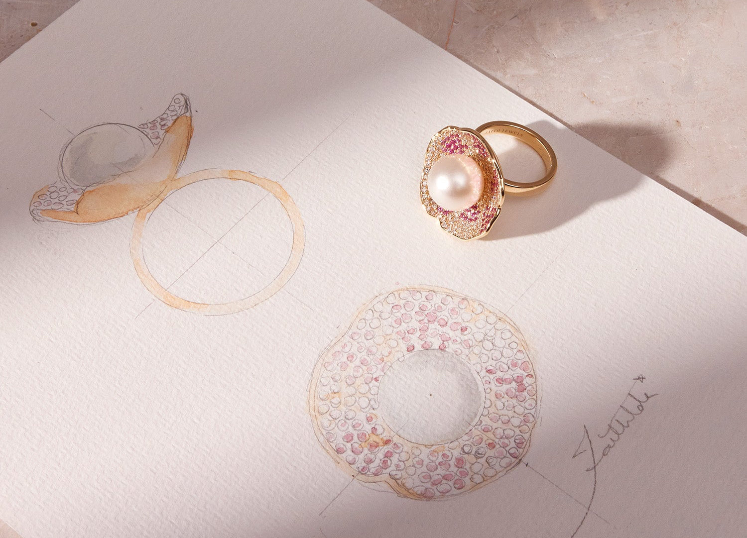 Flower gold ring with a pearl and pink gemstones and diamonds, on a hand-sketched drawing of a ring.
