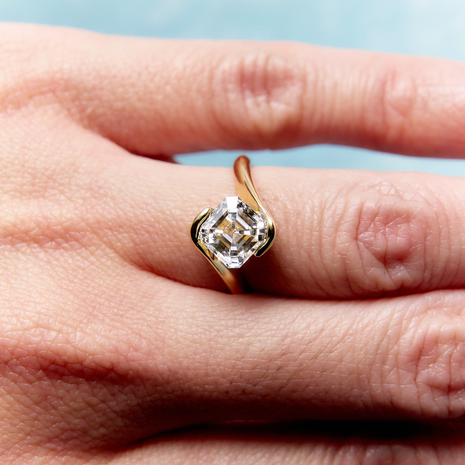 Engagement ring with asscher-cut diamond in two-tone gold setting, worn on finger