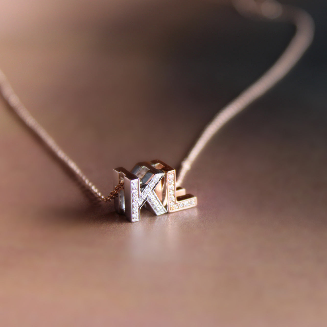 Bespoke pendant necklace with diamond-adorned initials "K" in white gold and "L" in rose gold on rose gold chain.