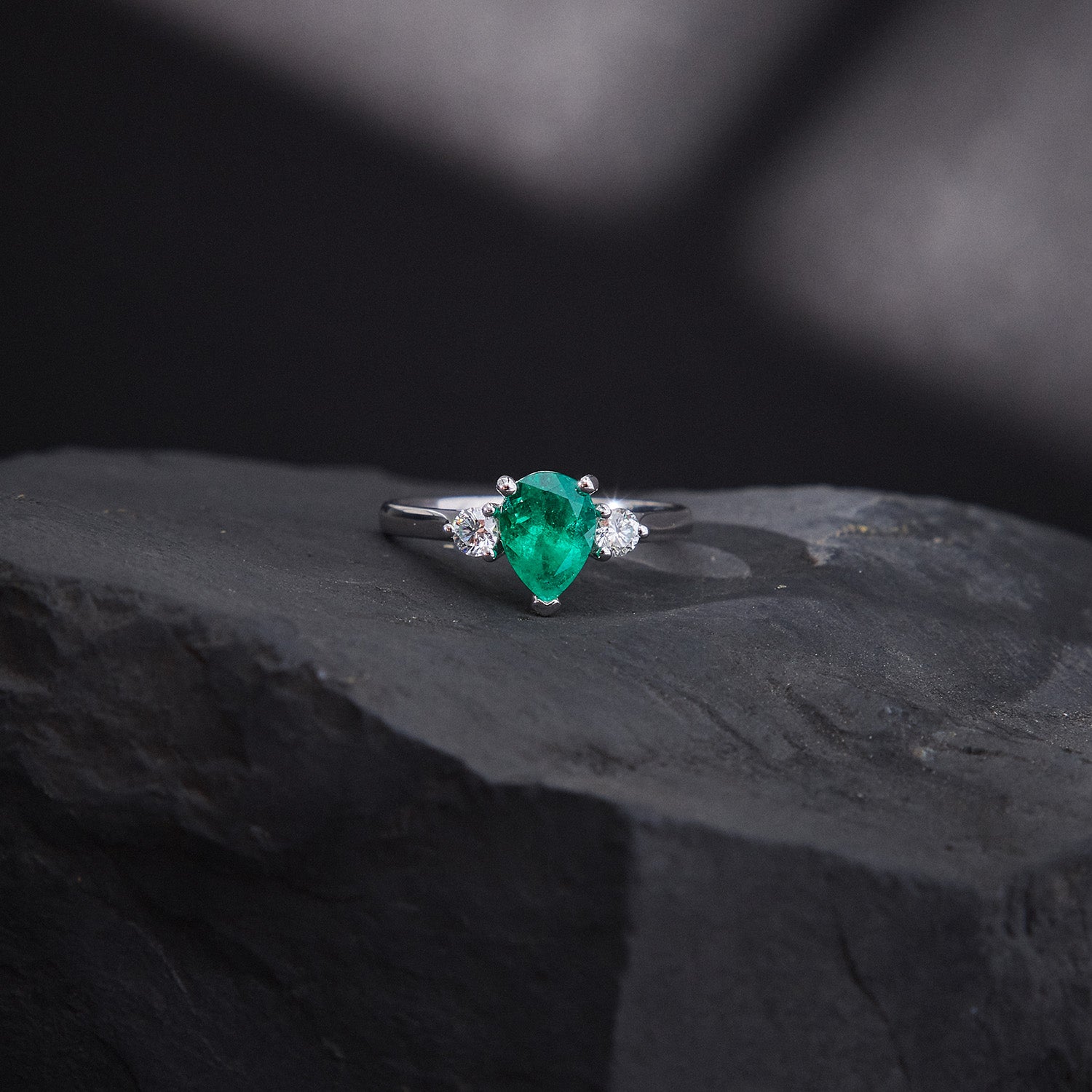 Pear-cut emerald trilogy ring with round white diamonds in 18k white gold, elegant and timeless design.