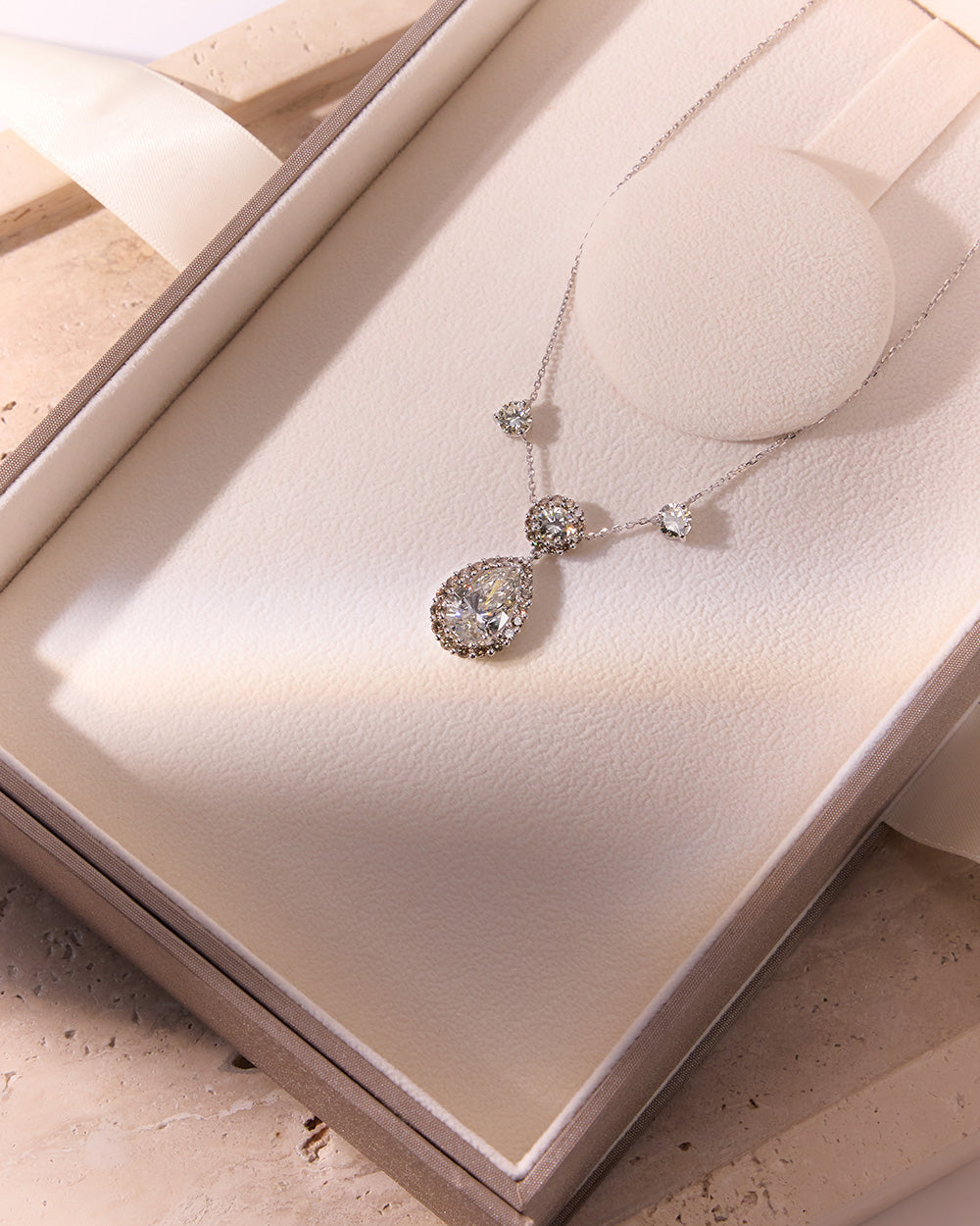 Elegant diamond necklace featuring round brilliant pendant with pear-shaped drop and champagne halo in Faith Jewels box
