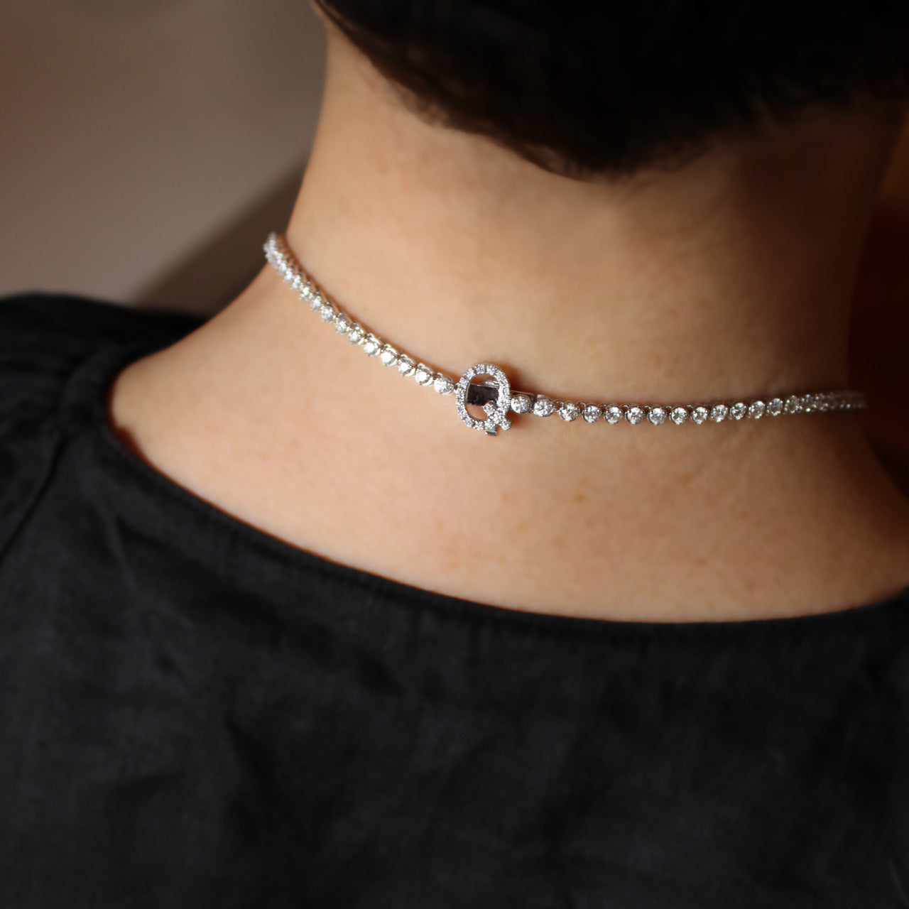Bespoke graduated diamond tennis necklace with “Q” initial clasp in elegant design, worn on model from the back.