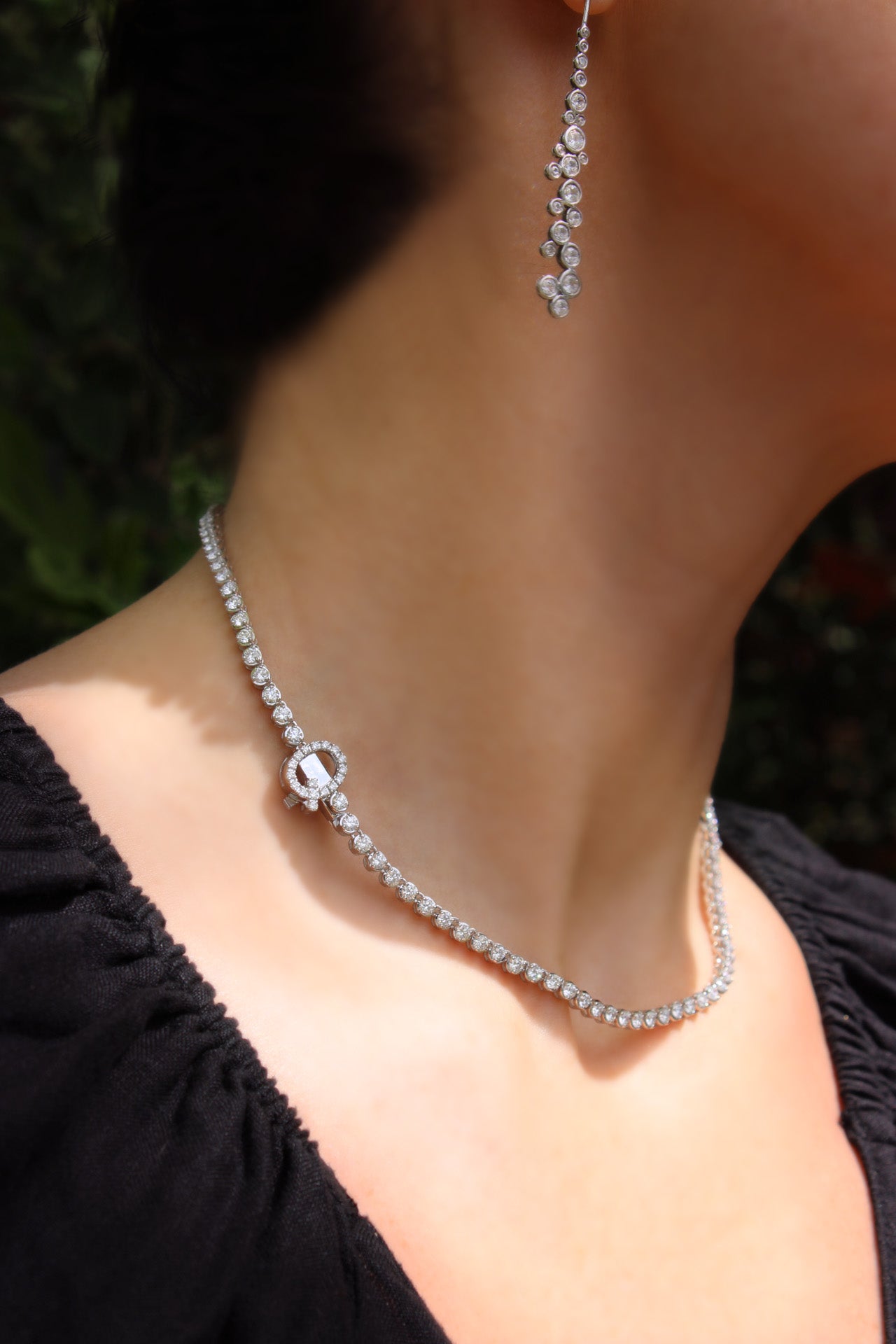 Bespoke graduated diamond tennis necklace with “Q” initial clasp in elegant design, worn on model with matching diamond earrings.