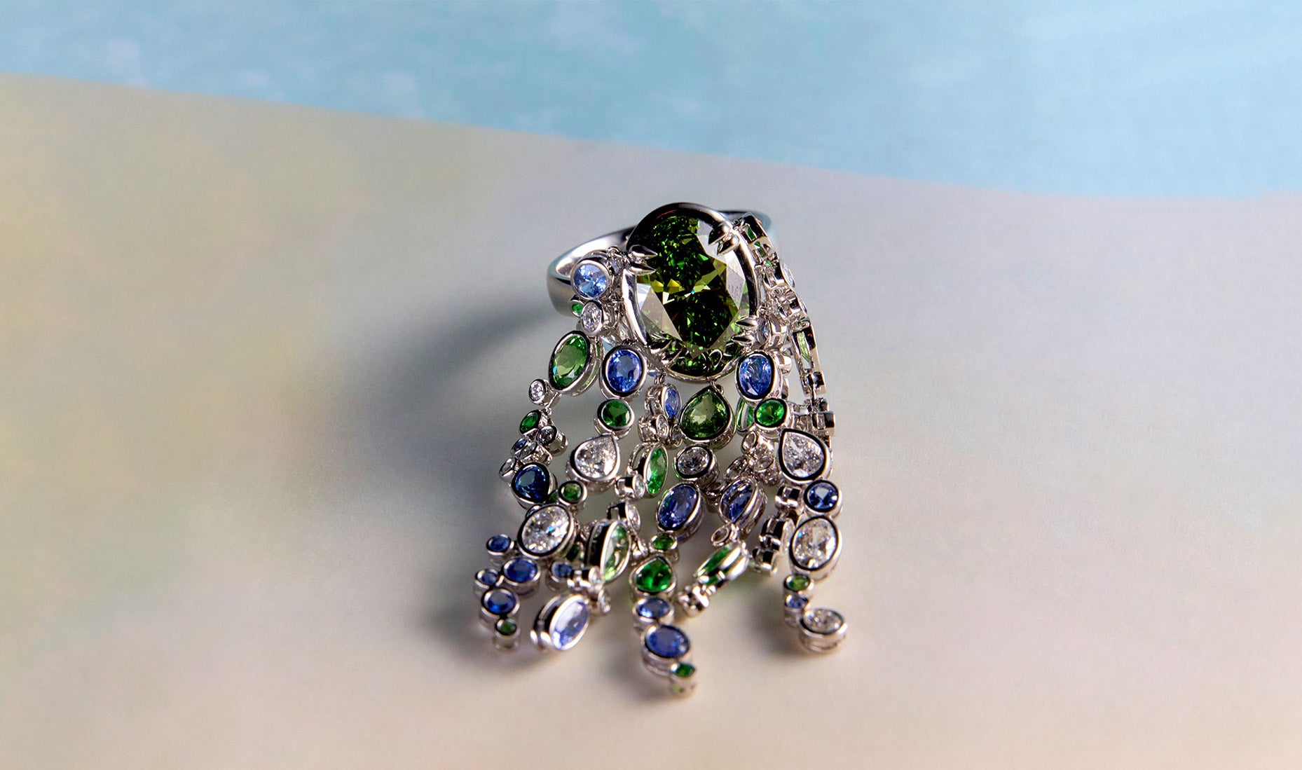Waterfall ring with streams of blue sapphires, green sapphires, and white diamonds cascade organically across the hand, echoing the rhythm of water catching light as it moves over stone.