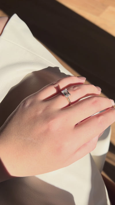 Emerald-cut East-West Engagement Diamond Ring in yellow gold with white gold claws, a modern yet timeless elegant design, worn on hand model.