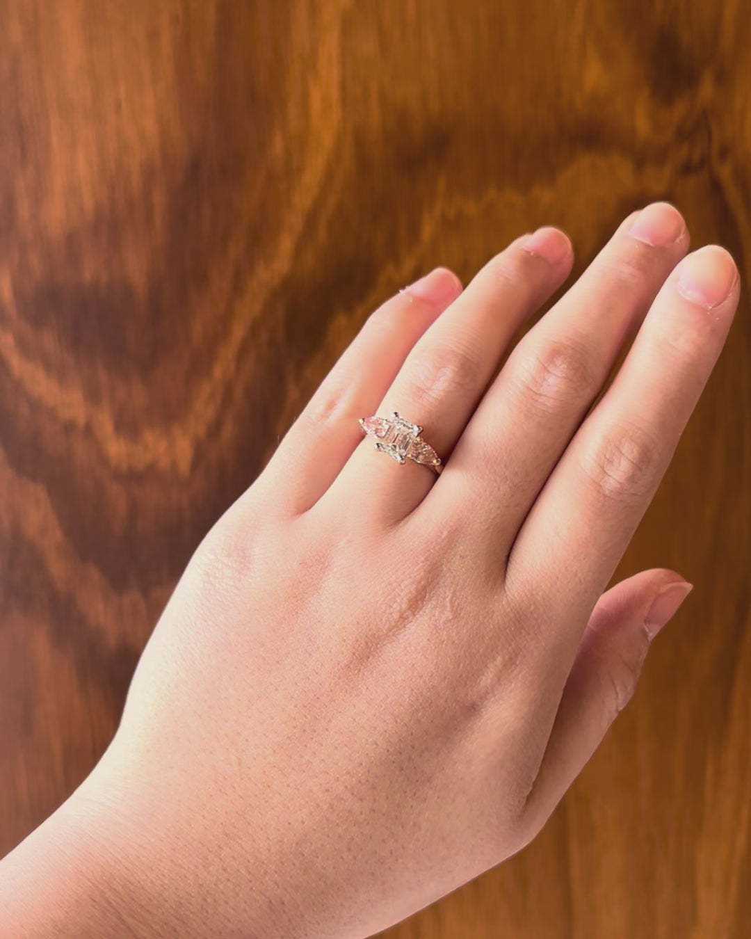 Bespoke trilogy engagement ring in 18k rose gold with emerald-cut diamond centre and pink diamond accents, elegant and timeless design, worn on hand model.