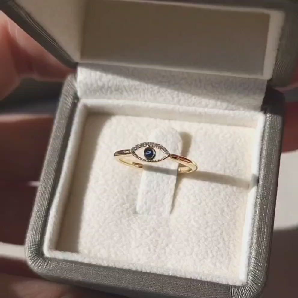 Faith Jewels Protection Ring featuring a yellow gold band with an evil eye design, accented by white diamonds and a central blue sapphire.