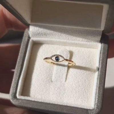 Faith Jewels Protection Ring featuring a yellow gold band with an evil eye design, accented by white diamonds and a central blue sapphire.